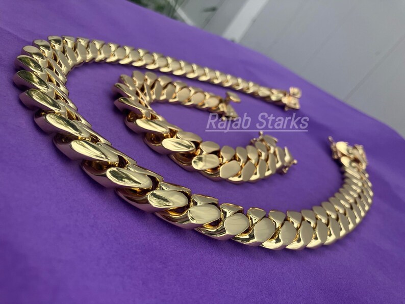 May include: A gold chain necklace and bracelet set with a thick, chunky curb link design. The set is made of gold-plated metal and features a shiny, polished finish.