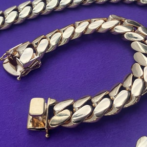 May include: A gold chain necklace with a curb link design. The chain is made of thick, interlocking links.