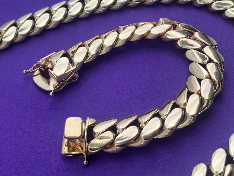 May include: A gold chain necklace with a curb link design. The chain is made of thick, interlocking links.
