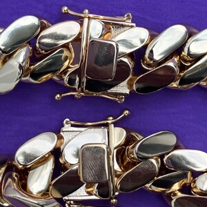 May include: Close-up of a two-tone gold chain with a clasp. The chain is made of alternating gold and silver links.