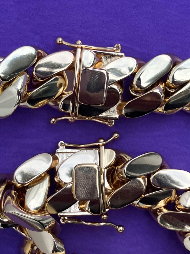 May include: Close-up of a two-tone gold chain with a clasp. The chain is made of alternating gold and silver links.