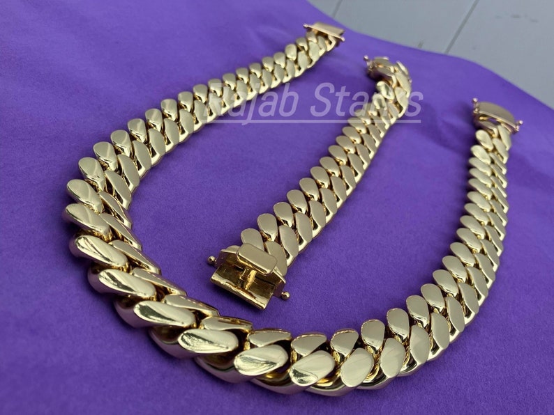 May include: Two gold-coloured curb chain necklaces, one longer than the other, on a purple background.