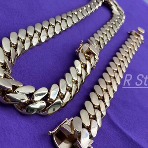 May include: A gold chain necklace and bracelet with a Cuban link style. The chain is thick and has a shiny finish.