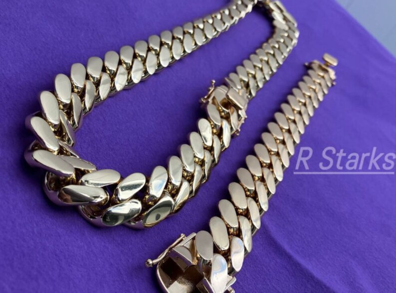 May include: A gold chain necklace and bracelet with a Cuban link style. The chain is thick and has a shiny finish.