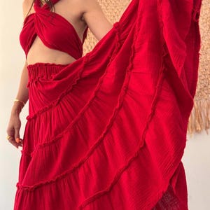 May include: A vibrant red two-piece set consisting of a halter-style crop top with a twisted front design and a matching high-waisted maxi skirt. The skirt features a gathered elastic waistband and multiple horizontal tiers with ruffled edges.