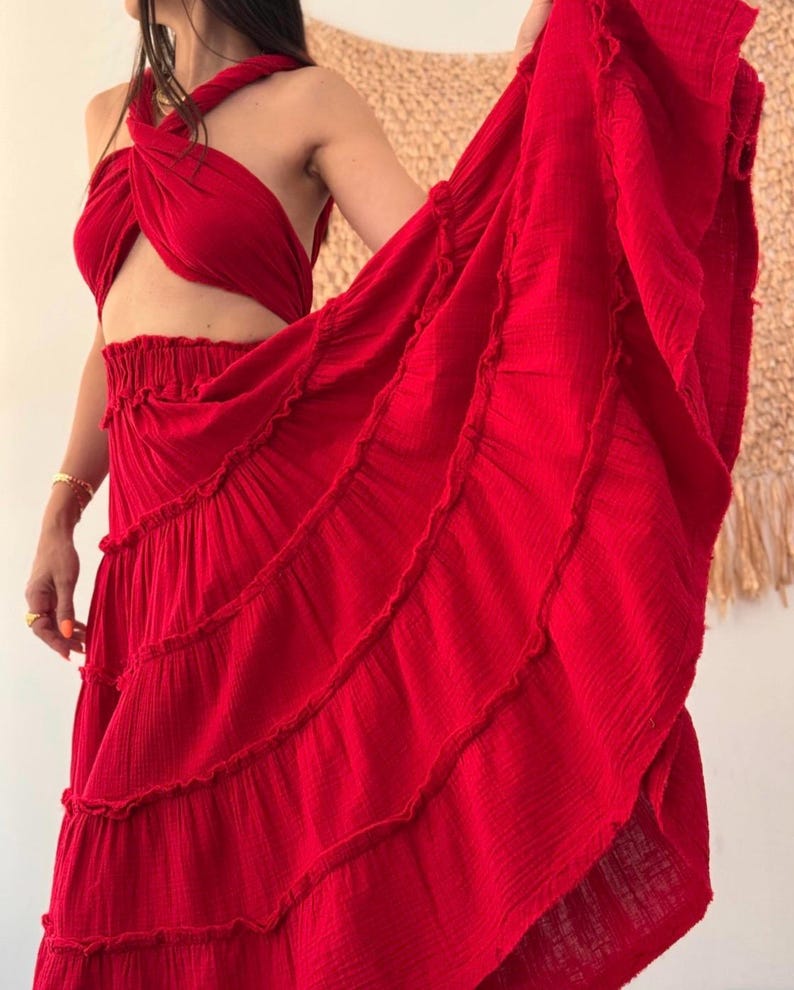 May include: A vibrant red two-piece set consisting of a halter-style crop top with a twisted front design and a matching high-waisted maxi skirt. The skirt features a gathered elastic waistband and multiple horizontal tiers with ruffled edges.