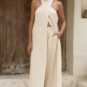 May include: A cream-coloured halter top and wide-leg trousers ensemble. The top has a wrap-around design, and the trousers feature a high waist and pockets. The outfit is made of a textured fabric, creating a flowing silhouette. Suitable for casual or resort wear.