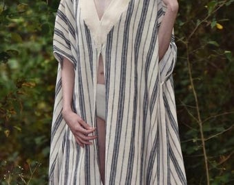 Puede incluir: Prenda larga a rayas verticales azules y blanco roto, con escote en V profundo y corte abierto. La tela parece ligera. El diseño es holgado y fluido, sugiriendo un estilo bohemio relajado. Las rayas verticales alargan la figura.