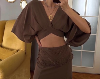 May include: A brown crop top with a V-neck and wide sleeves paired with a brown maxi skirt featuring a fringe detail and a side slit.