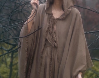 May include: A brown hooded cloak featuring a textured, frayed edge trim along the front opening and hood. The garment is made of a solid-colored fabric and drapes over the shoulders, providing a loose, open-front silhouette with a matching tie closure.