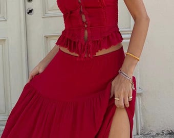 May include: A vibrant red two-piece set consisting of a sleeveless camisole top with thin straps, a ruffled hem, and a front lace-up detail, paired with a matching long, flowing skirt featuring a high side slit and an elasticized waistband.