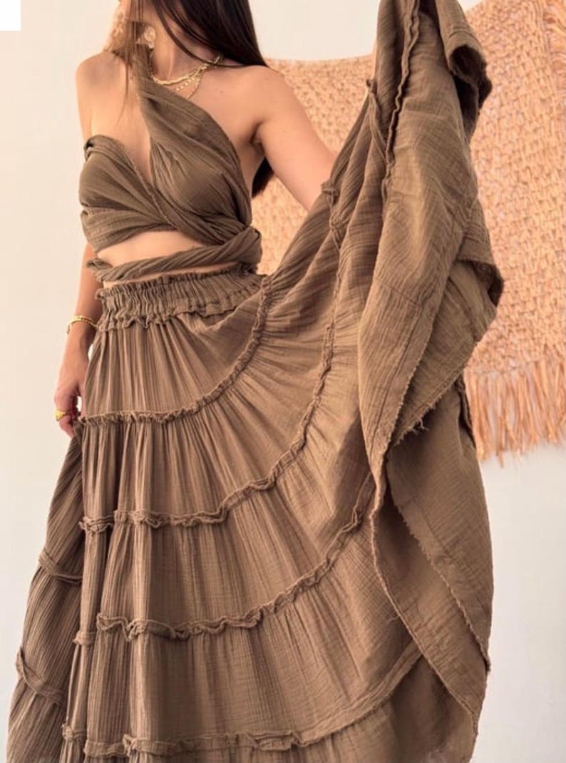 May include: A two-piece brown outfit featuring a halter top and a tiered maxi skirt. The top is a wrap style, and the skirt has a ruffled hem. The fabric appears to be a lightweight, textured material. The outfit is suitable for warm weather.Ritual Dress