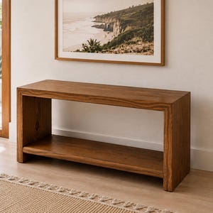 May include: A rectangular wooden console table featuring a medium brown finish with visible wood grain patterns. The piece has a flat top surface, two solid side panels, and a lower shelf that spans the entire width between the two side supports.