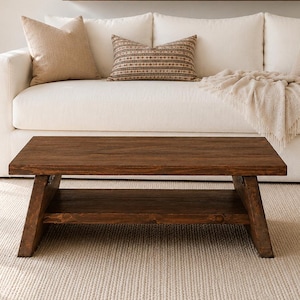 May include: A rectangular dark brown wooden coffee table with a lower shelf and angled legs. The table features a smooth, solid wood construction with a visible grain pattern, providing a sturdy surface for living room placement.