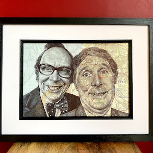 May include: A black and white framed print of two men's faces, created using a map of Leeds, England. The men are smiling and have a similar facial expression. The print is on a white background.