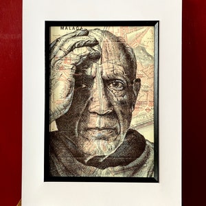 May include: A black and white drawing of a man's face, with a map of Malaga, Spain superimposed over it. The man's face is drawn in a realistic style, with details of wrinkles and lines. The map is in a vintage style, with faded colors and a worn look. The drawing is framed in a black frame and mounted on a white mat.