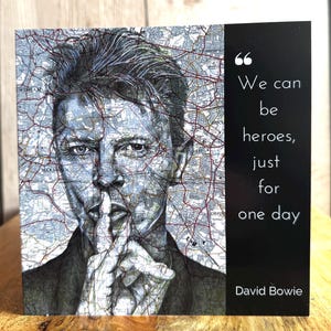 May include: A square art print featuring a portrait of David Bowie with a finger over his lips. The portrait is overlaid with a map design. Text on the right reads "We can be heroes, just for one day" and "David Bowie."