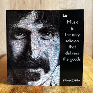 May include: A square art print featuring a portrait of Frank Zappa with a map overlay. The print includes the quote "Music is the only religion that delivers the goods" by Frank Zappa, in white text on a black background.