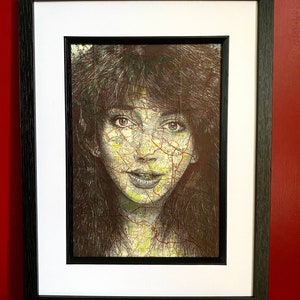 May include: A framed black and white portrait of a woman with long dark hair. The woman's face is made up of a map with yellow and red lines. The frame is black with a white mat.