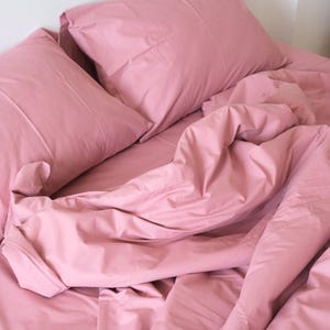 May include: A pink bed with a white headboard and two pink pillows. The sheets are rumpled and the comforter is pulled back.