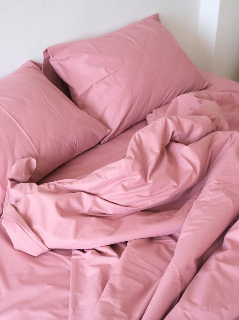 May include: A pink bed with a white headboard and two pink pillows. The sheets are rumpled and the comforter is pulled back.
