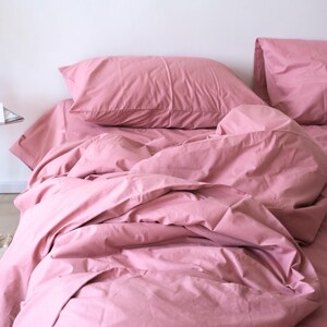 May include: A pink bed with a white headboard and two pink pillows. The bed is made with a pink duvet cover and the duvet is slightly rumpled.