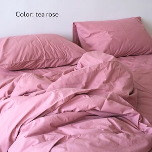 May include: A pink bed with a white wall in the background. The bed is made with a pink duvet and two pink pillows. The text "Color: tea rose" is visible in the image.