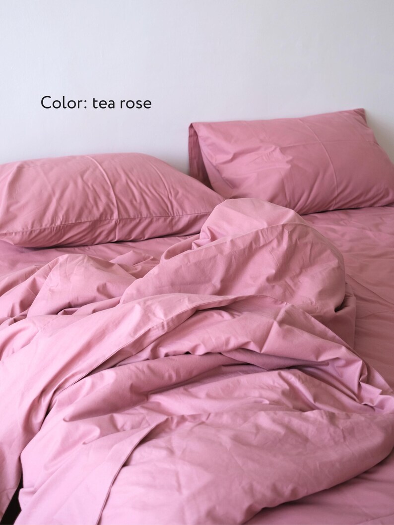 May include: A pink bed with a white wall in the background. The bed is made with a pink duvet and two pink pillows. The text "Color: tea rose" is visible in the image.
