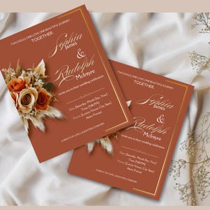 May include: Two wedding invitations with a rust-colored background and gold accents. The invitations feature a floral arrangement with dried flowers and grasses. The text on the invitations reads "Two souls one love one beautiful journey together."  "Sophia James & Rudolph McIntyre" and "invite you to their wedding celebration".
