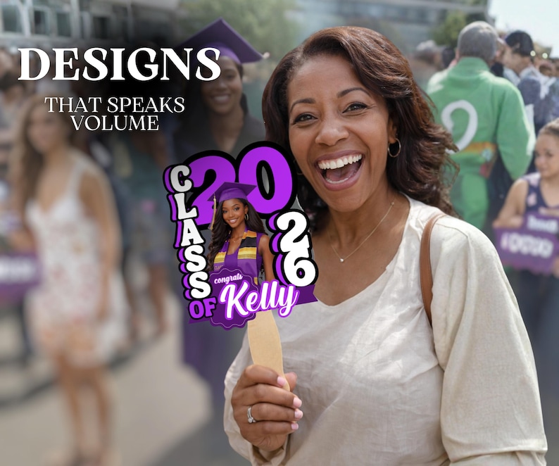 May include: A woman smiles while holding a graduation sign that says "Class of 2026" and "Congrats Kelly". The sign is purple and white with a photo of a graduate. The background includes other people.