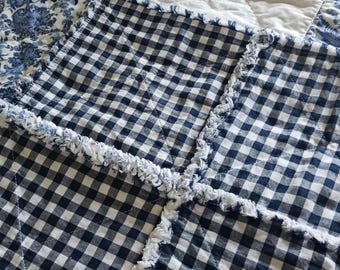 May include: A patchwork quilt featuring alternating squares of navy blue and white gingham check fabric and solid white fabric with diagonal quilting lines. The seams between the squares have exposed, frayed fabric edges creating a textured finish.