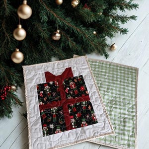 May include: Two rectangular quilted fabric mats. One mat features a central black square with a nutcracker pattern, accented by a dark red fabric bow design. The other mat has a light green and white gingham pattern. Both have swirl stitching.
