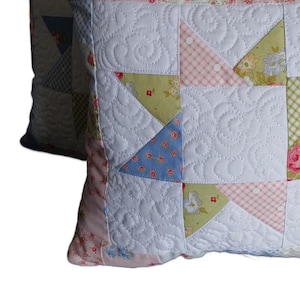 以下が含まれることがあります： パッチワークデザインの装飾用クッション2つ。クッションは、キルティング模様の白い背景と、ピンク、青、緑の花柄のカラフルな布の正方形が特徴です。縁は花柄の生地でトリミングされています。