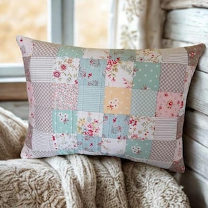May include: A rectangular throw pillow featuring a patchwork design composed of various fabric squares. The patterns include floral prints, small polka dots, and thin stripes in a color palette of soft pink, light blue, sage green, and cream.