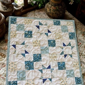 May include: A square patchwork quilt featuring a repeating star pattern in shades of blue, cream, and white. The fabric squares display floral and dotted prints, accented by solid dark blue star points and intricate swirling machine quilting.