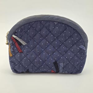 May include: A navy blue quilted cosmetic bag with a curved top and a zip closure. The bag has a diamond pattern with small white dots and colourful geometric accents. The zip pull has a small gold-coloured charm.