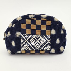 May include: A navy blue and beige patterned cosmetic bag. The bag features a woven checkerboard pattern and a geometric design. The bag has a zip closure and a small metal ball attached to the zip.