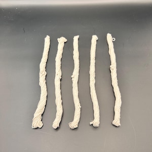 May include: Five strands of beige cotton cord, each approximately 25 cm long, are arranged in a row on a black surface.