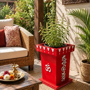 May include: A bright red square planter featuring a white Om symbol and a vertical white floral scroll design on the front. The top rim is decorated with a white triangular pattern, and the base is accented with a row of white dots.