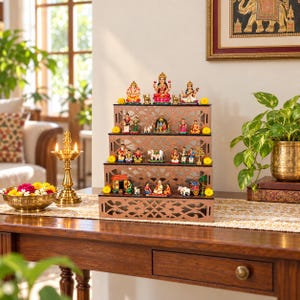 May include: A three-tiered wooden display stand with intricate laser-cut patterns, holding a collection of small, colourful Hindu deity figurines and miniature scenes arranged on each level, accented with small yellow marigold flowers.