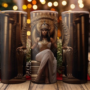 May include: Three gold and brown stainless steel tumblers with a design of a woman in a gold crown and white dress sitting on a throne. The woman is wearing gold jewelry and has a gold crown on her head.