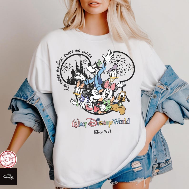 Puede incluir: Camiseta blanca con un gr&aacute;fico colorido de personajes de Disney, incluyendo Mickey Mouse, Minnie Mouse, Donald Duck y Goofy. El dise&ntilde;o incluye el texto "The Most Magical Place on Earth" y "Walt Disney World Since 1971".