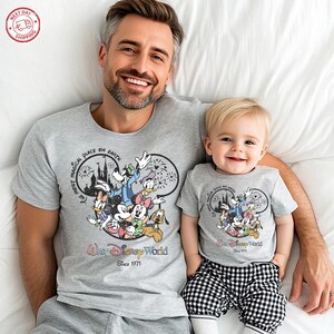 Puede incluir: Camisetas grises a juego con un dise&ntilde;o de Disney World con Mickey Mouse y sus amigos. Las camisetas tienen el texto "The Most Magical Place on Earth" y "Walt Disney World Since 1971". El ni&ntilde;o lleva pantalones a cuadros blancos y negros.
