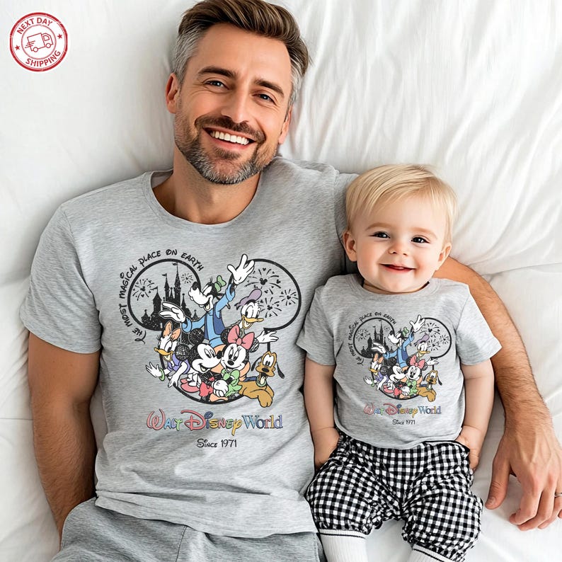 Puede incluir: Camisetas grises a juego con un dise&ntilde;o de Disney World con Mickey Mouse y sus amigos. Las camisetas tienen el texto "The Most Magical Place on Earth" y "Walt Disney World Since 1971". El ni&ntilde;o lleva pantalones a cuadros blancos y negros.