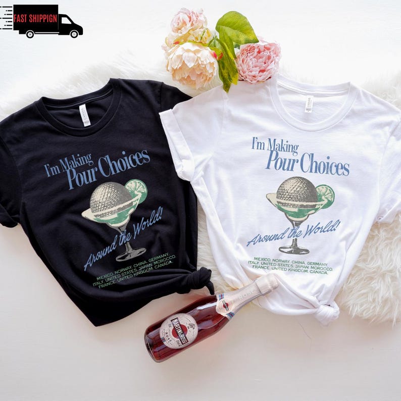 May include: Two t-shirts, one black and one white, with the text "I'm Making Pour Choices Around the World!" and a cocktail graphic. A bottle of red sparkling wine is in the foreground. Floral arrangement in the background.