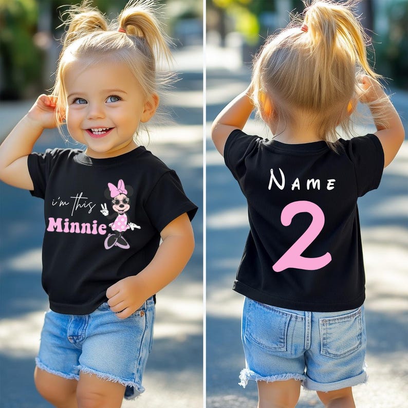 以下が含まれることがあります： ミニーマウスのグラフィックとピンク色の「I'm this Minnie」という文字が入った黒いTシャツ。Tシャツの背面には「NAME」という文字と数字の「2」がピンク色でプリントされています。子供は青いデニムのショートパンツを着用しています。