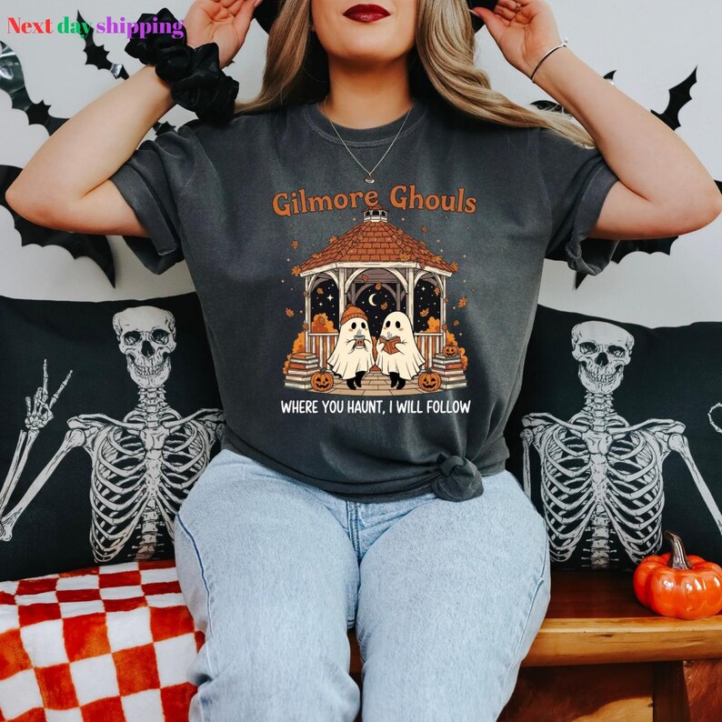 Puede incluir: Camiseta gris oscuro con un dise&ntilde;o tem&aacute;tico de Halloween. El dise&ntilde;o incluye un mirador con dos figuras de fantasmas, calabazas y el texto "Gilmore Ghouls, Where You Haunt, I Will Follow". La camiseta es c&oacute;moda.