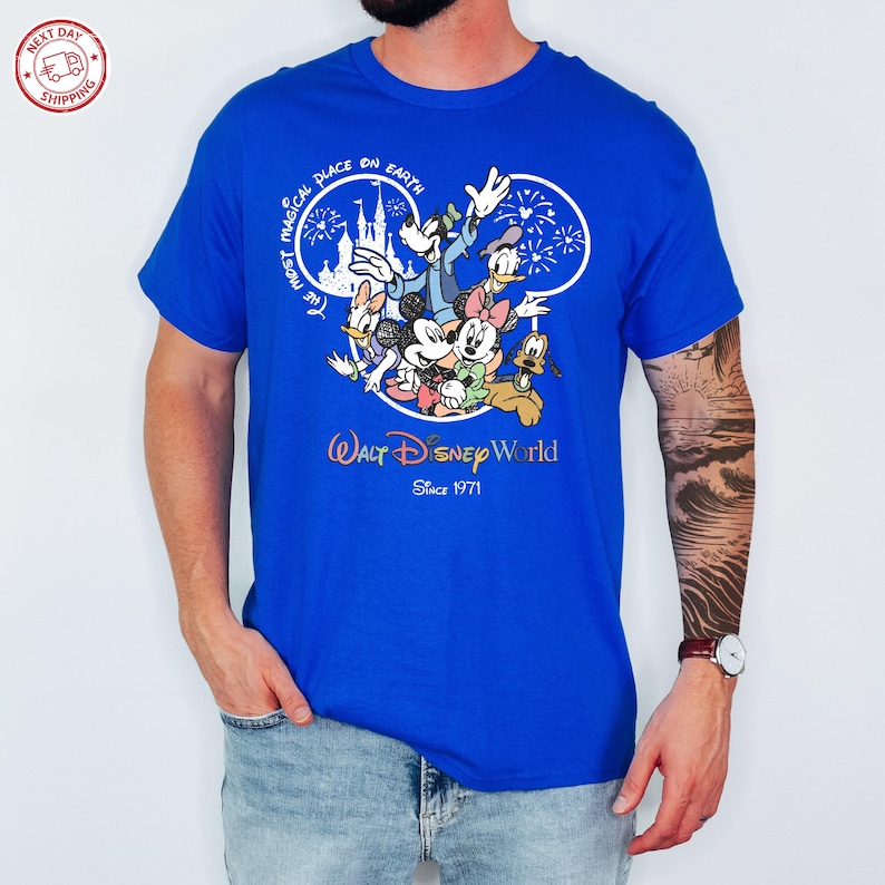 Puede incluir: Camiseta azul real con un dise&ntilde;o de personajes de Disney, incluyendo Mickey Mouse, Minnie Mouse, Donald Duck y Goofy. El dise&ntilde;o incluye el texto "The Most Magical Place on Earth" y "Walt Disney World Since 1971".