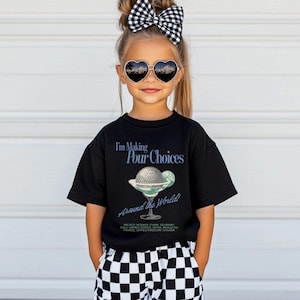May include: A black t-shirt with the text "I'm Making Pour Choices Around the World!" and a graphic of a cocktail. The shirt is worn by a child wearing heart-shaped sunglasses and a black and white checkered bow.