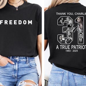 May include: Black t-shirt with the word "FREEDOM" in white block letters on the front. The back of the shirt features the text "THANK YOU, CHARLIE" above the number "31" with images and the text "A TRUE PATRIOT 1993-2025".